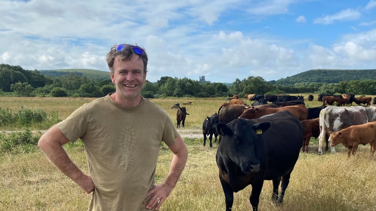 Jake Hancock, the farm tenant at Middlebere Farm, standing with cows to his right and Corfe Castle in the background.